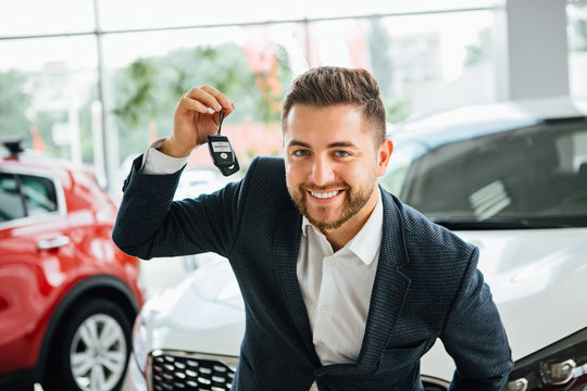 Man is holding a key of their new car, looking at camera and smiling.