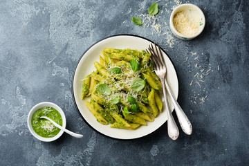 Penne rigate pasta with parmesan cheese and basil leaves in ceramic plate on gray vintage old concrete background. Selective focus.