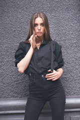Beautiful girl in black clothes oversize with suspenders. Dark background. Toned image.