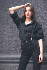 Beautiful girl in black clothes oversize with suspenders. Dark background. Toned image.