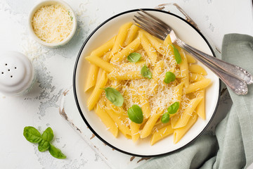 Penne rigate pasta with parmesan cheese and basil leaves in ceramic dish on light old concrete background. Selective focus.