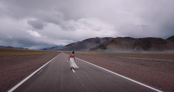 Abandoned bride walking in the middle of the highway, mountain landscape. Aerial view, 4k