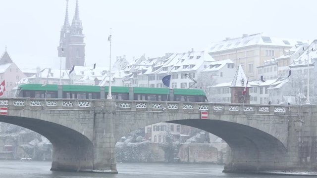 Tram crossing a bridge in a snowy urban environment from the right to the left side