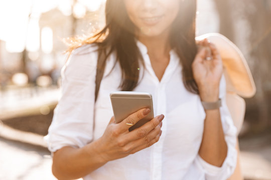 Cropped image of Smiling brunette woman in shirt using smartphone