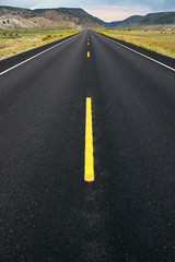 Long and straight Country road with yellow road marking and hills in background. Photographed from middle of the road.