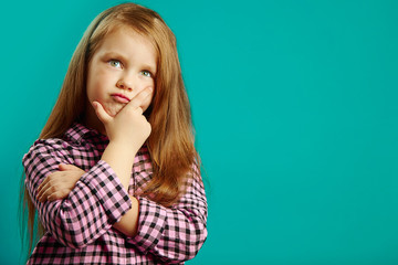 Beautiful portrait of pensive little girl on isolated blue background, looks up, has a focused...