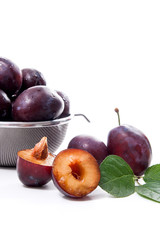 Steel colander with ripe plums, whole and half ripe plums with leaf isolated on a white background..