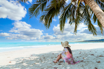 young female sitting on tropical beach and relaxing at summer time