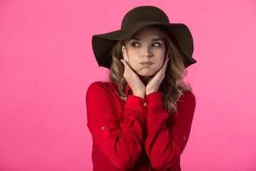 beautiful young girl in a red shirt and hat on a pink background with puffed cheeks