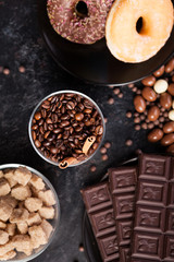 Coffee beans in a glass with cinnamon sticks next to different types of candies on a dark vintage wooden background