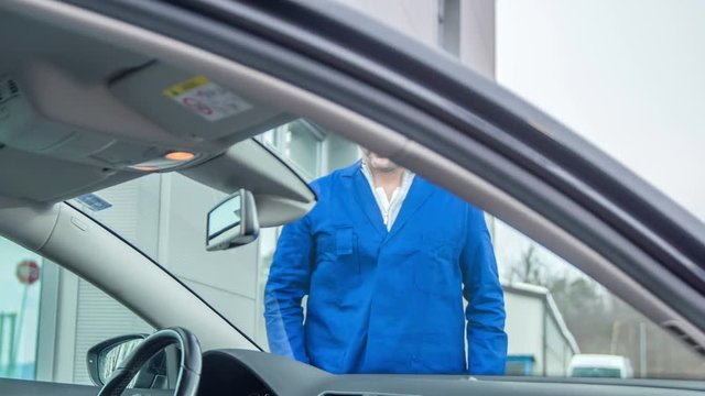 A young man touches the crack on the front window of the car and he is annoyed about it.