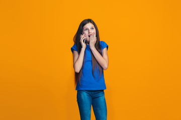 The happy teen girl standing and smiling against orange background.