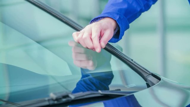 A young man is checking the crack on the front window of the car. He is annoyed when he sees it.