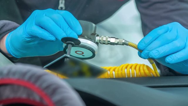 A young man is checking the crack on the front window of the car. He is wearing special blue gloves.