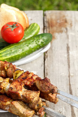 shish kebab on skewers. On a wooden table with fresh vegetables. kebab on the background of green grass
