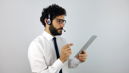 Handsome consultant of call center in headphones with a tablet on gray background. Young and brunette man looking at tablet.