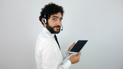 Handsome consultant of call center in headphones with a tablet on gray background. Young and brunette man smiling looking at camera.