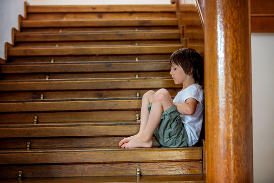 Sad child, sitting on a staircase in a big house, concept for bullying