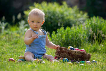 Cute child, playing with little bunny and easter eggs in a blooming garden, springtime