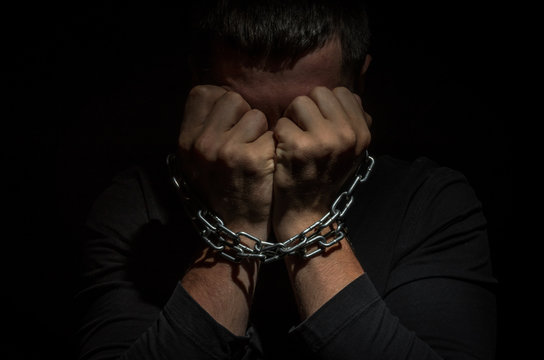 A man prisoner chained in a chain clinging to his head against a black  background Photos | Adobe Stock