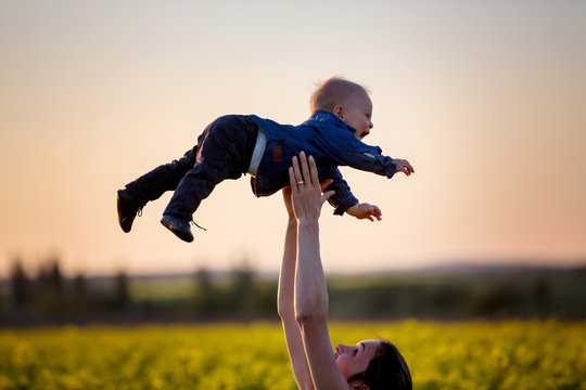 Young mother holding up her todller son in canola field