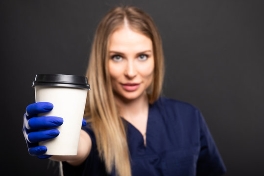Beautiful female doctor wearing scrubs drinking takeaway coffee.