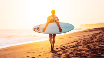 Silhouette of surfer walking on the beach near the ocean with surfboard