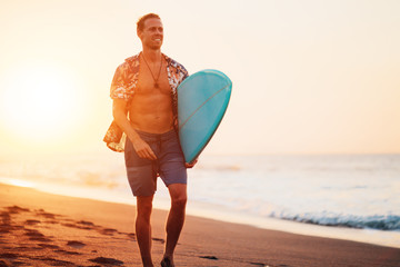 Fototapeta na wymiar Guy surfer walking on the beach near the ocean with short surfboard at sunset