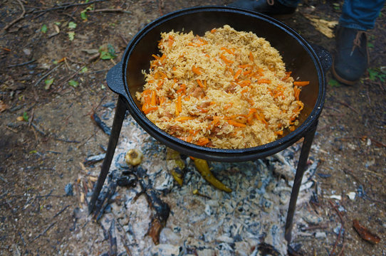 Meat with rice and carrot in a cauldron over a bonfire