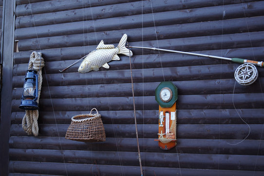Fishing tools hanging on the dark wood wall. Set of equipment with rod, fish, barometer, basket and lantern with rope