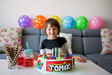 Cute child, boy, celebrating his birthday with colorful cake, candles, balloons