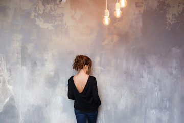 Obraz premium Woman standing in front of grungy concrete back to camera. Loft edison lights hanging from ceiling