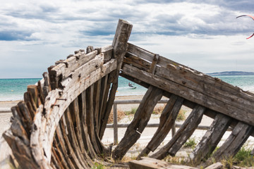 Fototapeta na wymiar Kitesurf front a old medieval boat's casing on the beach of Spain with beautiful sky landscape and blue sea in the background