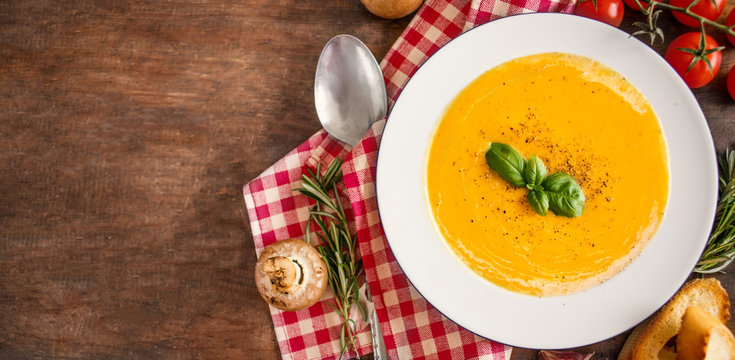 Cream soup with  Pumpkin and Carrot  on Red classic Checkered tablecloth on wooden rustic table. Squash Soup with herbs. Top view. Copy-space.