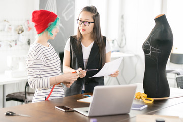 Waist up portrait of two contemporary creative fashion designers collaborating on project planning work standing by tailors table with sewing dummy in modern atelier studio