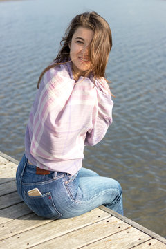 smiling woman on a wooden jetty looking at camera covering herself from the cold