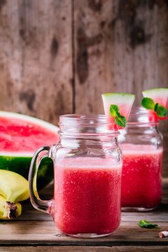 Watermelon and banana smoothie in mason jars with mint on wooden background