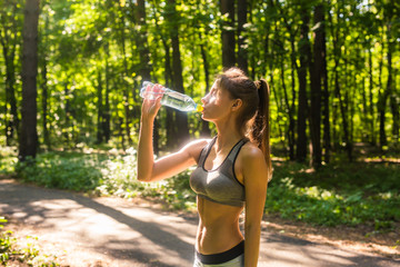 Fitness beautiful woman drinking water and sweating after exercising on summer hot day in park. Female athlete after work out.