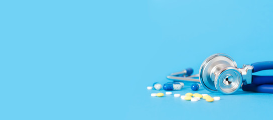 Stethoscope and pills on blue background copy space