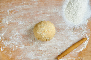 Raw dough with rolling pin and scattered flour on the wooden kitchen table. Baking background. Top...