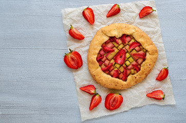 Fototapeta na wymiar Strawberry tart with rhubarb on the gray kitchen table with copy space. Vegetarian galette decorated with fresh strawberries. Tasty summer dessert. Top view