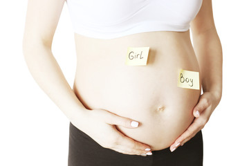 Close up of pregnant woman wearing white supportive seamless maternity bra & black yoga pants with boy & girl stickers on bare belly. 9th month of pregnancy. Expectancy concept. Background, copy space