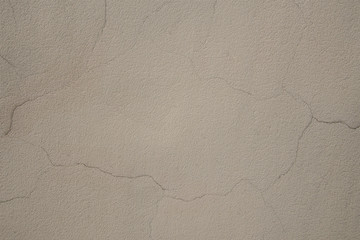 The texture of the wall is covered with decorative plaster with a lot of cracks. Cracks on the plastered wall. Beige surface with small cracks.