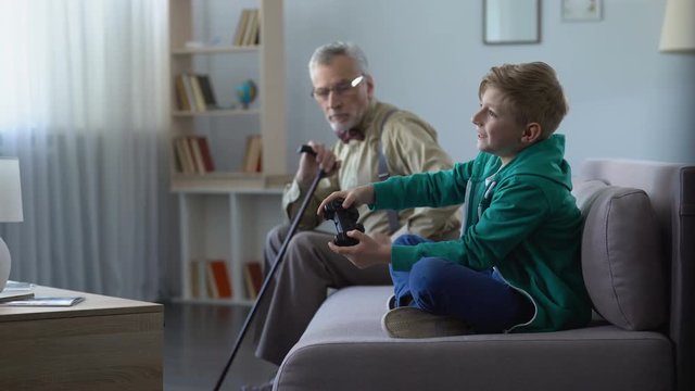 Dissatisfied grandpa looking at happy grandson playing video game generation gap