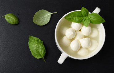 Mini mozzarella with herbs, basil on ablack stone background top view