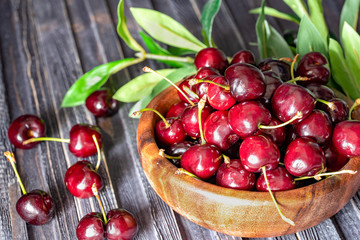 Fresh sweet cherries in plate on dark wooden background with copy space. Summer and harvest concept.