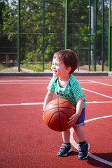 a boy of two years playing with a ball on the basketball court. Toddler boy playing basketball