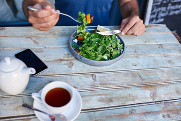Man sitting at a rustic wooden table eating delicious salad 