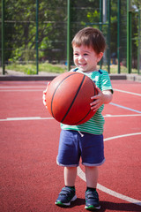 a boy of two years playing with a ball on the basketball court. Toddler boy playing basketball