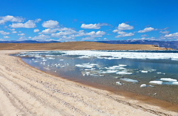 A beautiful spring landscape with a sandy beach and ice floes on the blue clear water of the Siberian Lake Baikal on a May sunny day